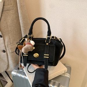 Vintage black messenger bag with gold clasp and horse charm on a travel suitcase