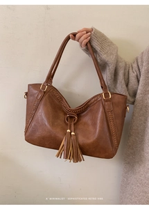 Detail showing the brown faux leather tote bag with fringe charm and woven stitching