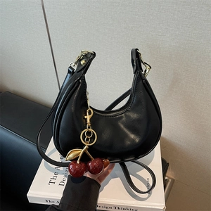 Retro black crescent shoulder bag with golden cherry charm on white books