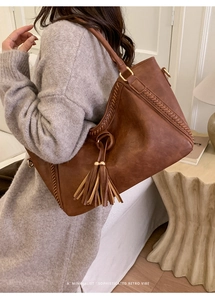 Close-up of caramel brown leather tote bag with stylish fringe detail and braided stitching
