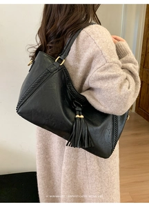 Detail of black retro tassel tote bag with lychee texture and wide braided shoulder strap