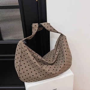 Brown polka dot corduroy hobo bag shown hanging on a door handle in a minimalist room