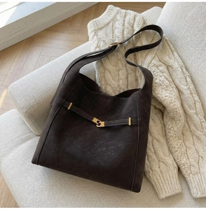 Macro shot of dark brown faux suede material and gold metal buckle on a shoulder bag
