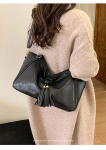 Detail of a black retro tote bag with fringes on a model wearing a beige sweater