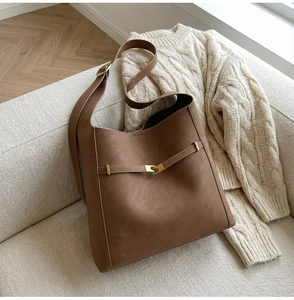 Detail of coffee brown matte suede tote bag with golden buckle on a beige sofa