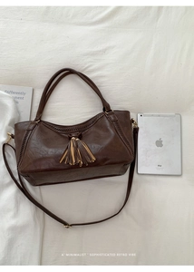 Detail of dark brown faux leather tote bag with fringe and braided edge near a tablet