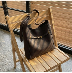 Detailed view of brown matte leather shoulder bag with gold buckle on wooden chair