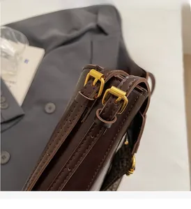 Detail view of glossy brown leather bucket bag side with gold square adjustment buckles