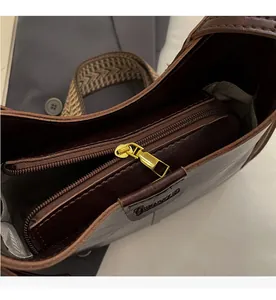 Detailed macro of smooth gold zipper and wide woven shoulder strap on brown bucket bag