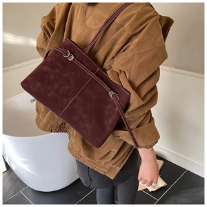 Detail view of burgundy suede tote bag with contrast white stitching and slender strap