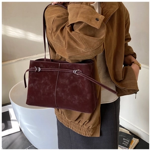 Macro view of burgundy suede tote bag featuring a decorative buckle and slim shoulder strap