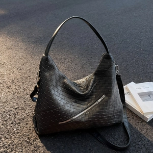 Large black woven leather hobo bag with diagonal silver zipper on an asphalt background