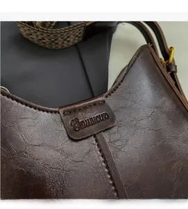 Detail of dark brown leather handbag featuring embossed logo and retro cracked texture