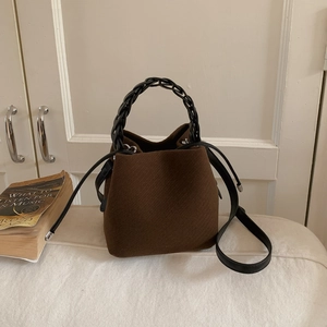 Brown bucket bag with black woven handle and crossbody strap in a minimalist home setting