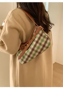 Detail of green plaid shoulder bag with adjustable brown leather strap and gold eyelets