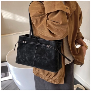 Detail of black suede tote bag featuring white contrast stitching and decorative buckle