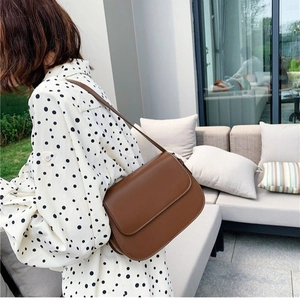 Close-up of minimalist brown leather shoulder bag with flap closure on a model