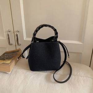 Minimalist dark blue bucket bag with black woven handles and leather shoulder strap