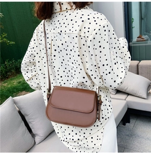 Detail of vintage brown crossbody flap bag with adjustable strap on model's shoulder