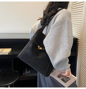 Detail of black suede tote bag with golden metal ring closure and smooth leather strap