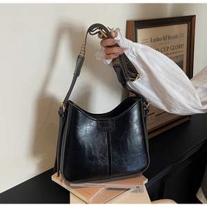 Detail of black faux leather bucket bag with embossed logo and jacquard woven strap
