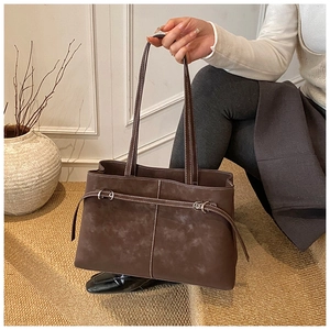Detail of dark brown suede tote bag with decorative silver buckle and white stitching