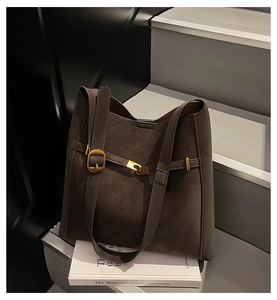 Detail of dark brown faux suede tote bag with golden buckle on minimalist stairs