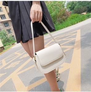 Detail of a creamy white leather shoulder bag featuring a smooth flap and curved base