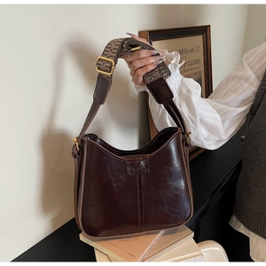 Detail of dark brown leather handbag with geometric jacquard wide shoulder strap and gold buckle