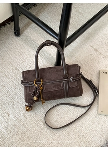 Détail du sac à main marron en daim mat avec coutures blanches et breloque clé