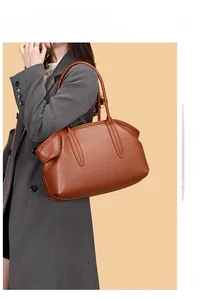 Detail of brown lychee grain leather bowling bag held by a model in a grey coat