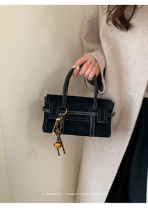 Détail d'un sac à main en daim noir avec coutures blanches contrastées et bijoux