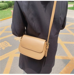 Detail of khaki leather crossbody bag with adjustable strap worn over a black coat