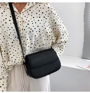 Detail of minimalist black crossbody bag with gold buckle and adjustable strap