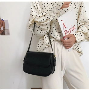 Detail of minimalist black leather flap bag with gold adjustment buckles and sleek shoulder strap