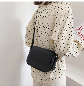 Side view of a vintage black leather crossbody bag with elegant gold hardware on a model
