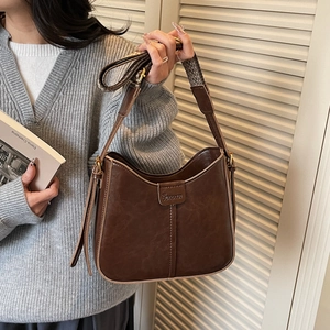 Detailed view of brown oil-wax leather shoulder bag with metallic logo and adjustable strap