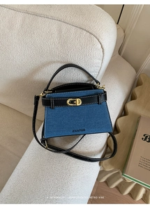 Detail of blue denim and black leather handbag with gold twist lock on a white sofa