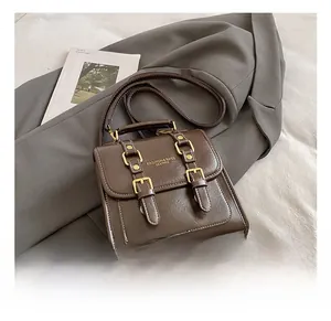 Détail d'un sac à dos vintage en cuir marron posé sur un costume gris avec magazines