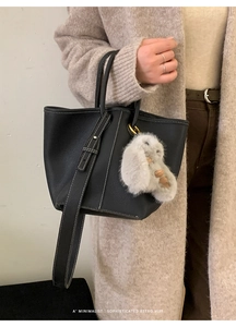 Close-up of black litchi grain leather tote with white stitching and plush bunny pendant