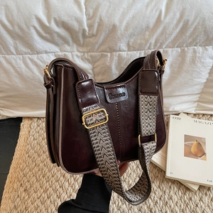 Close-up of retro dark brown leather underarm bag with logo and wide woven shoulder strap