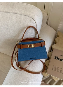 Detail of blue denim and brown leather handbag with gold twist lock on a white sofa
