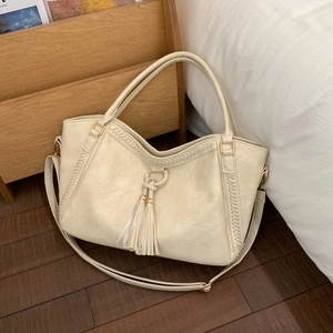Chic cream white fringe tote bag with wavy edges and adjustable strap on wood floor
