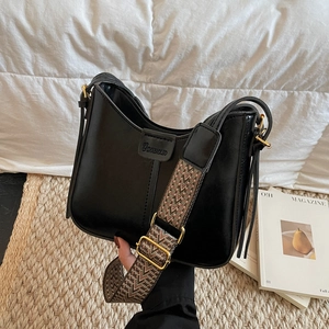 Detail of black crossbody bag with wide woven strap and golden metal hardware