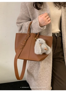 Brown litchi grain leather tote bag with white stitching and plush rabbit charm detail