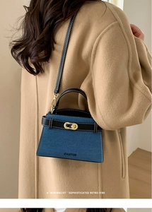 Detail view of retro denim shoulder bag with leather trim on model in tan wool coat