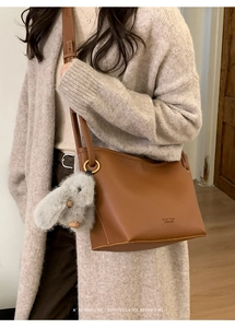Detail of brown leather bucket bag with gold logo and cute plush bunny charm accessory