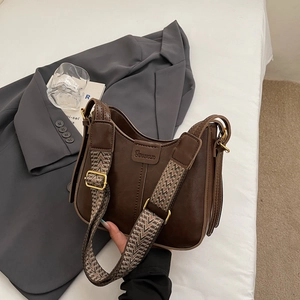 Detail of dark brown faux leather saddle bag with woven strap on a blazer background