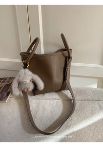 Detail of dark brown lychee leather bucket bag with cute plush bunny charm and golden ring
