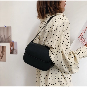 Minimalist matte black vintage shoulder bag worn by model against a clean wall background